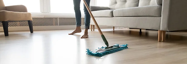 Person wischt Holzboden mit Wischmopp.